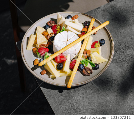Delicious cheese platter with fruits and nuts served on a sunny outdoor table Delicious cheese platter with fruits and nuts served on a sunny outdoor table 133807211