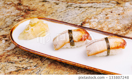 Sushi with pieces of grilled fish is artfully arranged on a simple white plate Sushi with pieces of grilled fish is artfully arranged on a simple white plate 133807248