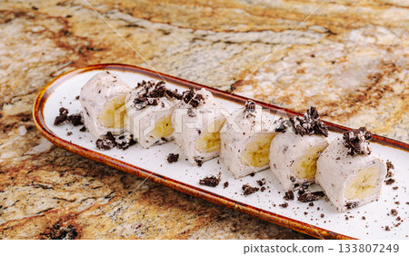 Delicious dessert roll with banana and crushed cookies on a plate 133807249