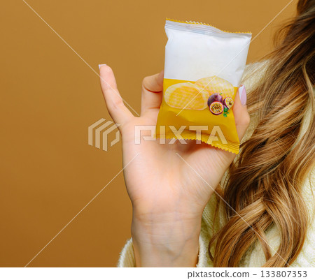 Woman holding a snack pack with fruity flavors against a warm background Woman holding a snack pack with fruity flavors against a warm background 133807353