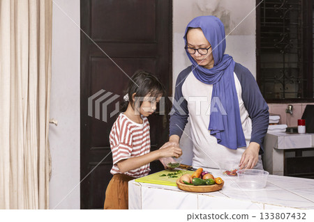 Indonesian woman and a child are cutting vegetables together in the kitchen for cooking Indonesian woman and a child are cutting vegetables together in the kitchen for cooking 133807432