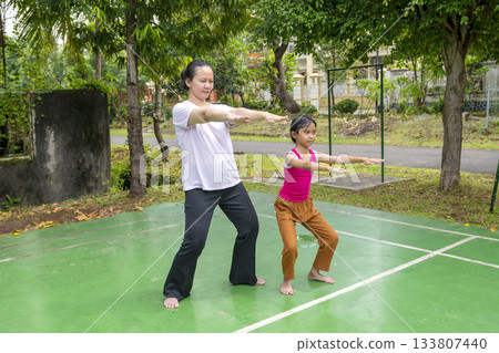 Woman and a child are practicing yoga on a green court Woman and a child are practicing yoga on a green court 133807440