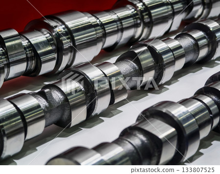 Close view of multiple shiny camshafts displayed against a bright background emphasizing their detailed craftsmanship and mechanical design Close view of multiple shiny camshafts displayed against a bright background emphasizing their detailed craftsmanship and mechanical design 133807525