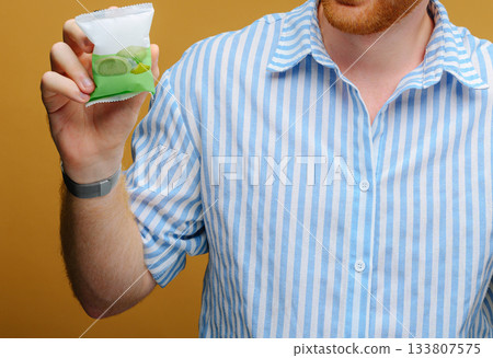 Holding a vibrant green jelly dessert in a striped shirt against a warm backdrop 133807575