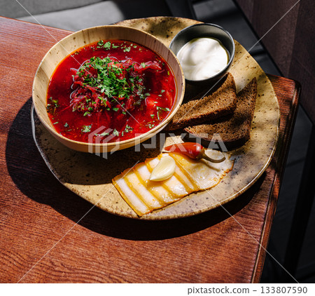 Hearty borscht served with fresh bread, cheese, and sour cream on a wooden table 133807590