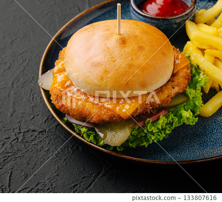 Crispy chicken burger with cheese served alongside golden fries 133807616