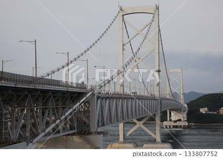 A close-up of the Naruto Kaikyo Bridge with cars passing by, the sea of the strait, and the land and sky of Shikoku A close-up of the Naruto Kaikyo Bridge with cars passing by, the sea of the strait, and the land and sky of Shikoku 133807752