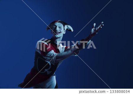 Jester reaching forward on dark blue stage with engaging theatrical expression Jester reaching forward on dark blue stage with engaging theatrical expression 133808034