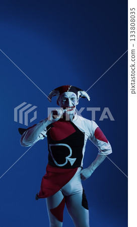 Jester biting poker chip on blue stage with humorous attitude 133808035