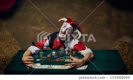 Jester leaning over poker table embracing chip stacks with wide excited face 133808044