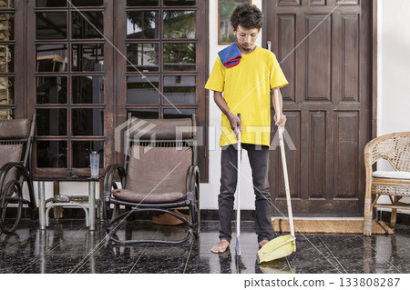 Young man in a yellow shirt is cleaning the floor with a broom. Cleaning concept 133808287