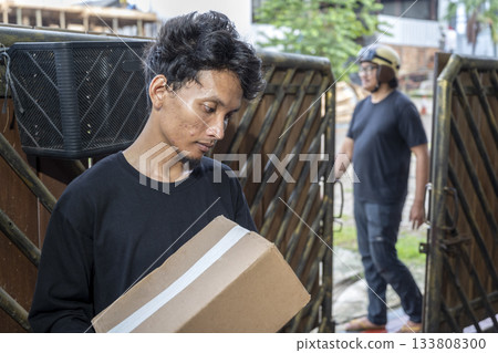 Indonesian southeast asian man receives a cardboard package from a delivery person wearing a helmet. Delivery service 133808300