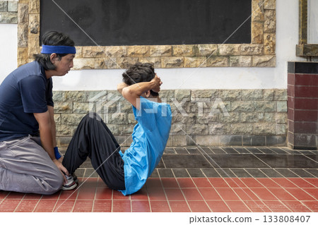 Asian man is helping a boy do sit ups 133808407