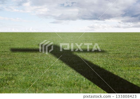 Shadow of cross-shaped structure is casting across grass field under cloudy sky, in flat design Shadow of cross-shaped structure is casting across grass field under cloudy sky, in flat design 133808423