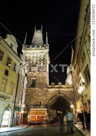 Showing 2D flat medieval gateway arch rising above cobbled road casting lamp glow on moving figures 133808453