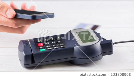 Flat design POS terminal is resting on light wood surface with card inserted and smartphone tapping Flat design POS terminal is resting on light wood surface with card inserted and smartphone tapping 133808908