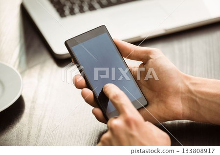 Smartphone is being tapped in flat design on wooden tabletop with laptop and cup, copy space 133808917