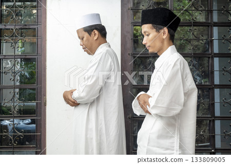 Two Indonesian southeast asian muslim men dressed in traditional white clothing and a cap while praying (Salat) 133809005