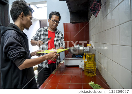 Two Indonesian southeast asian men inside a kitchen while preparing a meal together. Chopped ingredients on a chopping board Two Indonesian southeast asian men inside a kitchen while preparing a meal together. Chopped ingredients on a chopping board 133809037