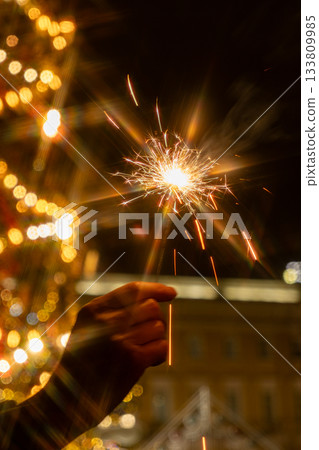hand holding sparkler in front of Christmas tree. picture shows festive and joyful mood. 133809985