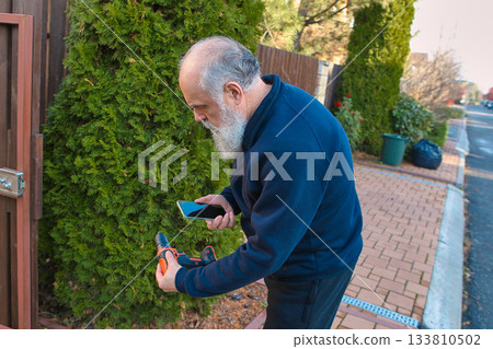 Senior man taking a photo of a drill outdoors with thoughtful focus 133810502