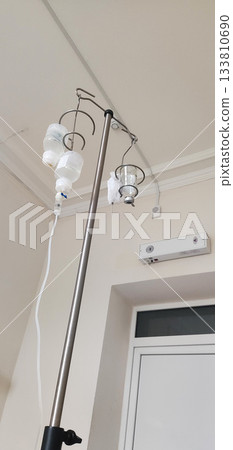 Intravenous drip stand with multiple fluid bags in medical room; healthcare equipment for patient treatment and recovery; essential apparatus for hospital care and medication delivery 133810690