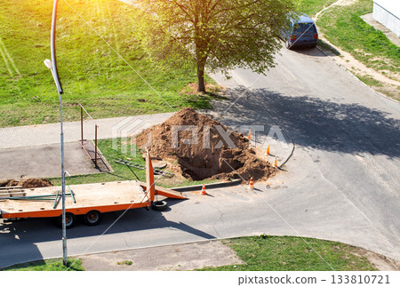 A dug hole in the city near the road. Concept of works on elimination of water channel leakage, laying pipes, repair works in the water supply system. Copy space for text 133810721
