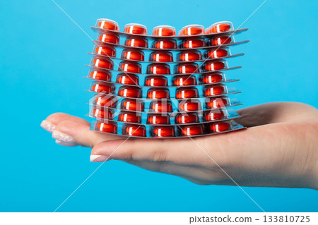Stack of pills on the palm of the hand on a blue background, close-up. Concept of vitamins in pharmaceuticals, close-up Stack of pills on the palm of the hand on a blue background, close-up. Concept of vitamins in pharmaceuticals, close-up 133810725