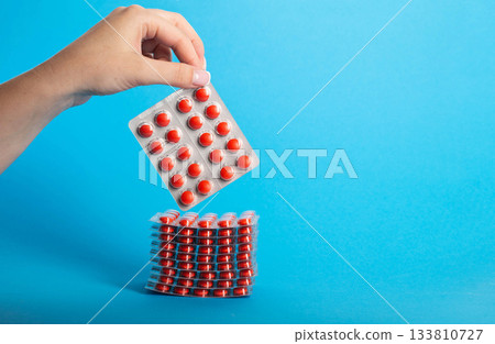 Female hand holding a blister pack with red pills on a blue background. Concept of lozenges for cough and sore throat, close-up. Copy space for text, treatment 133810727