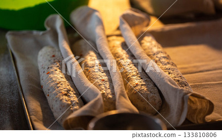 Unbaked bread dough baguettes covered with cloth, rising on baking sheet, preparation of homemade bakery goods, uncooked raw loaves ready for oven, kitchen cooking process 133810806
