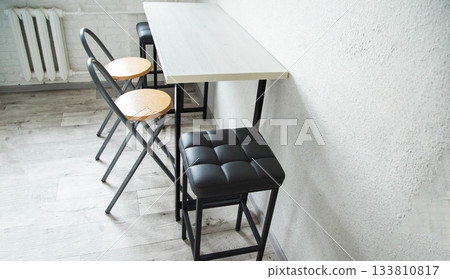 A compact table with stylish black upholstered chairs and stools in the kitchen, interior A compact table with stylish black upholstered chairs and stools in the kitchen, interior 133810817