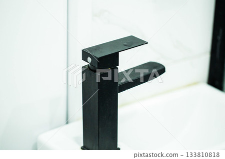 Black modern water faucet against white tiles and washbasin, close-up Black modern water faucet against white tiles and washbasin, close-up 133810818