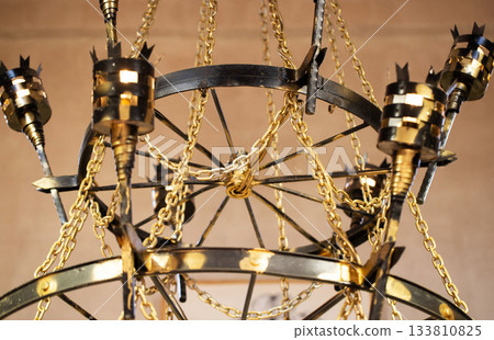 A beautiful antique wrought iron chandelier with chains hangs from the ceiling. Retro style, handmade 133810825