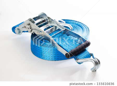 Blue ratchet strap coiled on white background. Heavy duty cargo tie down equipment with metal hooks and tensioner. Safety and securing load tool 133810836