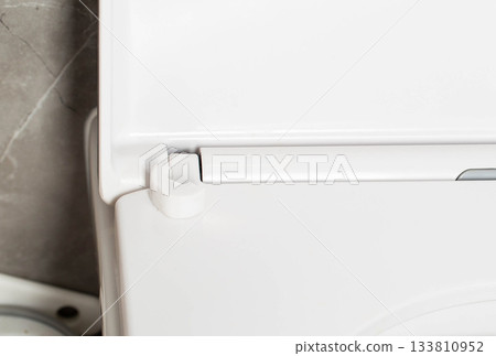 Broken hinge of a white toilet seat, close-up, low-quality plastic, industry Broken hinge of a white toilet seat, close-up, low-quality plastic, industry 133810952