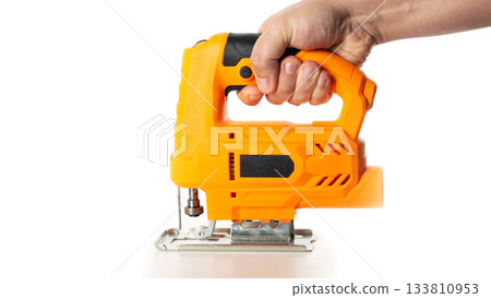 A yellow electric jigsaw in a worker's hand against a white background, isolated, close-up. Woodworking tool, industry A yellow electric jigsaw in a worker's hand against a white background, isolated, close-up. Woodworking tool, industry 133810953