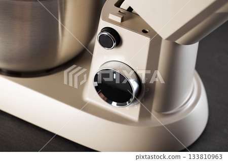 Cream color stand mixer appliance with stainless steel bowl and control dials on display, kitchen equipment for baking and food preparation 133810963