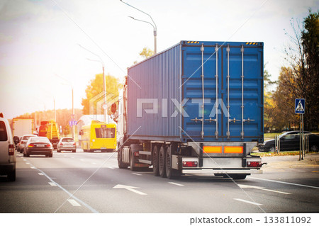 Blue semi-trailer truck with shipping container travels multi-lane road. Other vehicles on highway, urban transport concept. 133811092
