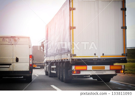 Rear view of truck trailer and delivery van on highway. Road transport and logistics concept during daytime with bright sky 133811093