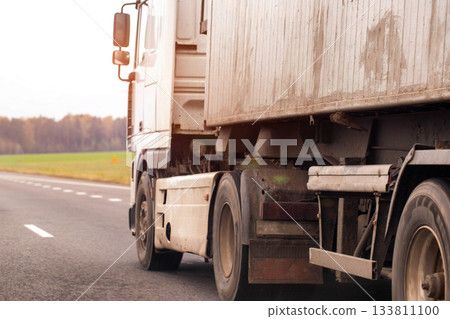 White heavy duty semi truck driving on asphalt road during day. Large commercial vehicle transport logistics cargo delivering goods across vast open landscape. 133811100