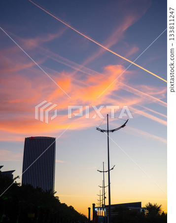 Construction of a multi-storey building against the backdrop of the sunset sky. Construction at the resort. Landscapes of Batumi. A developing place. Construction industry. Airplane tracks in the sky. 133811247