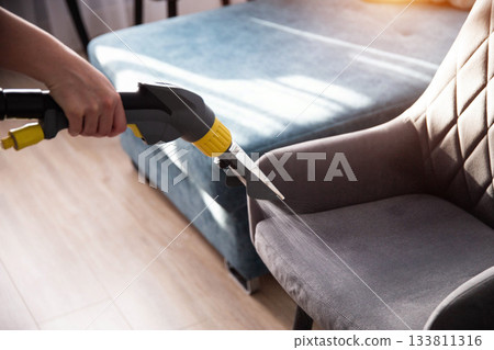 Cleaning a fabric chair using a steam cleaner in a well-lit living room during the afternoon 133811316