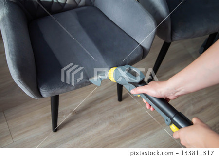 Cleaning upholstery on a chair with a vacuum attachment in a modern indoor space Cleaning upholstery on a chair with a vacuum attachment in a modern indoor space 133811317
