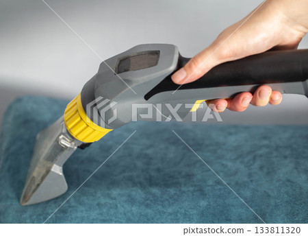 Cleaning a blue sofa with a steam cleaner for effective stain removal at home during the afternoon 133811320