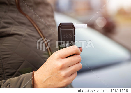 Female Hand Holds Portable Alcometer With Display. Checking Sobriety Next To Automobile. Copy space for text Female Hand Holds Portable Alcometer With Display. Checking Sobriety Next To Automobile. Copy space for text 133811338