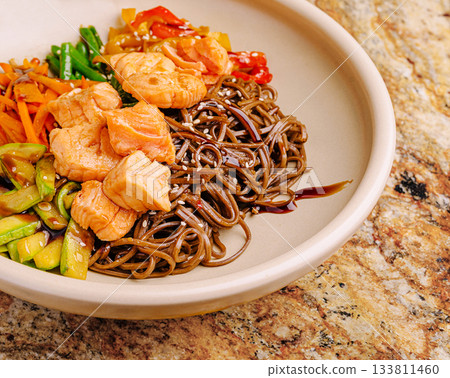 Salmon and soba noodle bowl with colorful vegetables on a textured surface 133811460