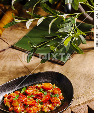 Fresh tomato dish served on a black plate with greens in a rustic setting Fresh tomato dish served on a black plate with greens in a rustic setting 133811473