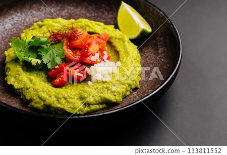 Delicious green avocado dip served with fresh toppings and lime wedge Delicious green avocado dip served with fresh toppings and lime wedge 133811552