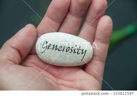 Hand holding a white stock with Generosity text engraved on it. Hand holding a white stock with Generosity text engraved on it. 133811597