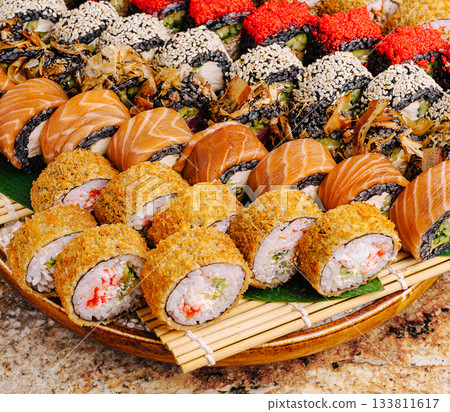 A colorful assortment of sushi rolls is arranged on a large wooden tray A colorful assortment of sushi rolls is arranged on a large wooden tray 133811617